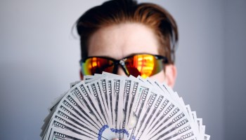 man in black framed sunglasses holding fan of white and gray striped cards